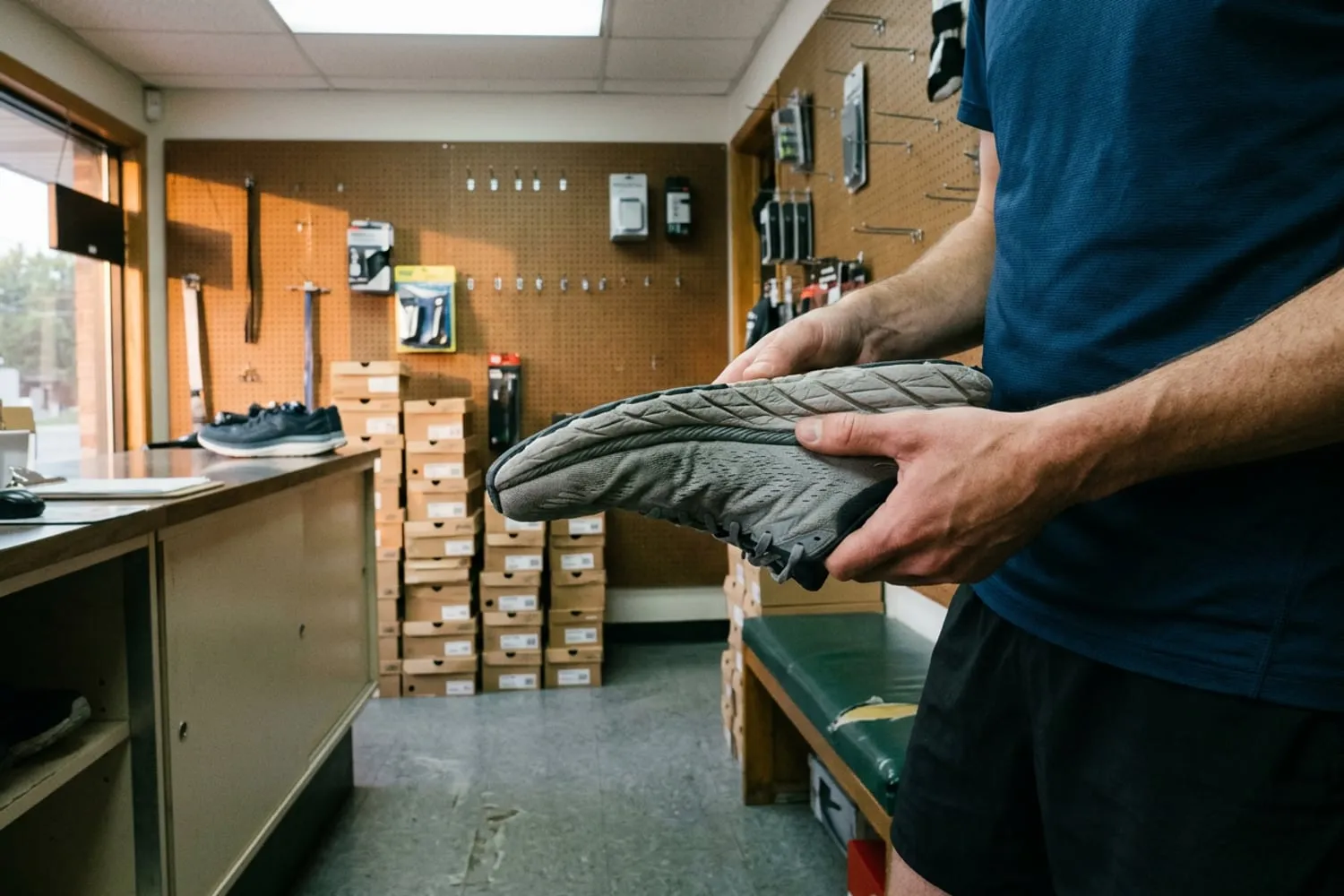 A runner’s thumb pressing into the creased foam midsole of a worn running shoe held sideways, deep wrinkles running along the foam